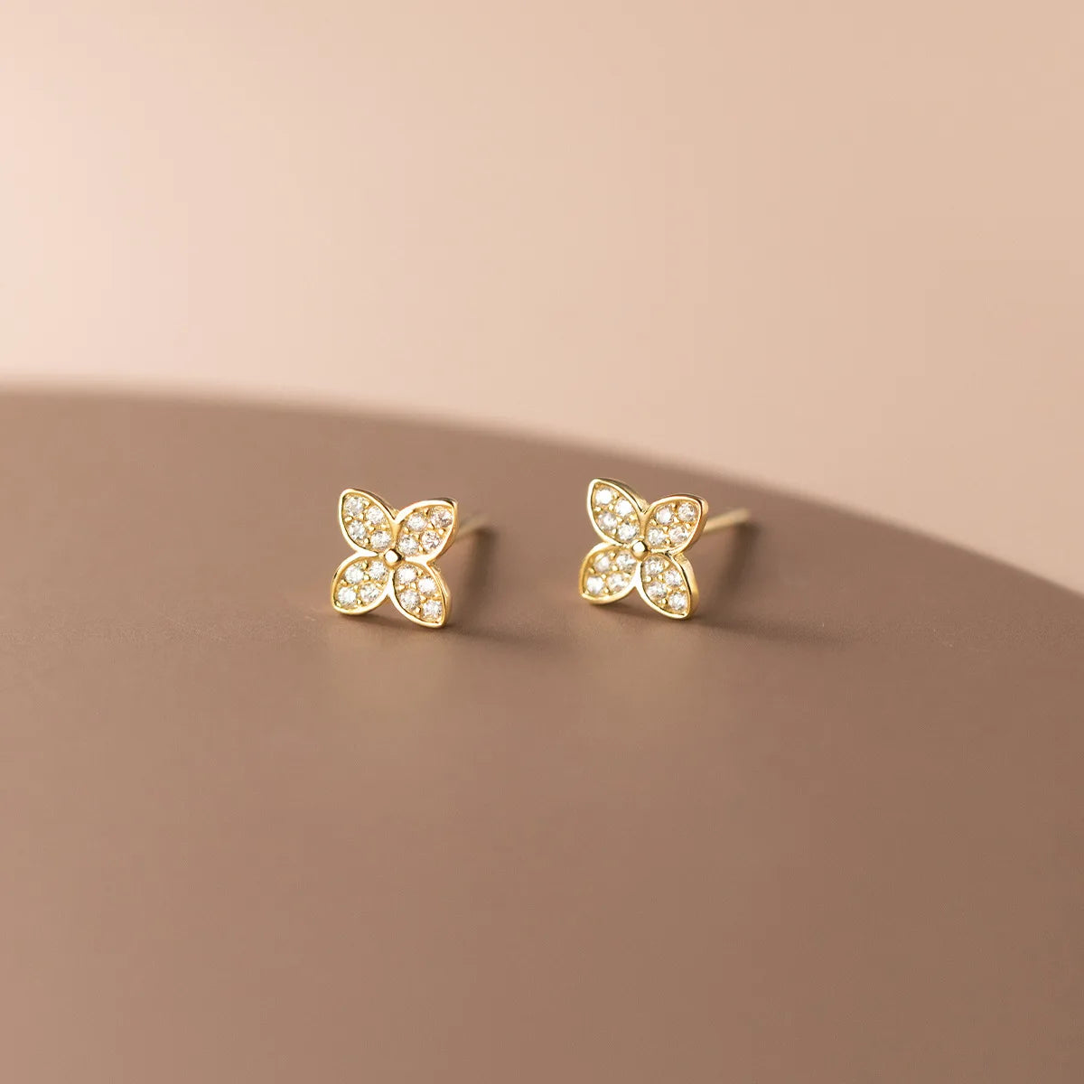 A pair of gold butterfly stud earrings with clear pavé stones, displayed on a clean, warm beige surface.