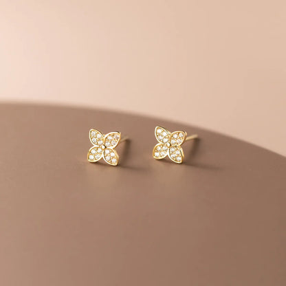 A pair of gold butterfly stud earrings with clear pavé stones, displayed on a clean, warm beige surface.