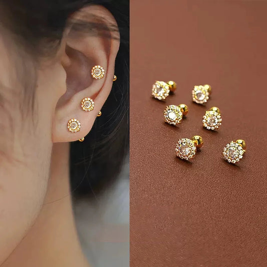 Gold earrings with clear stones worn on an ear and displayed on a brown surface.