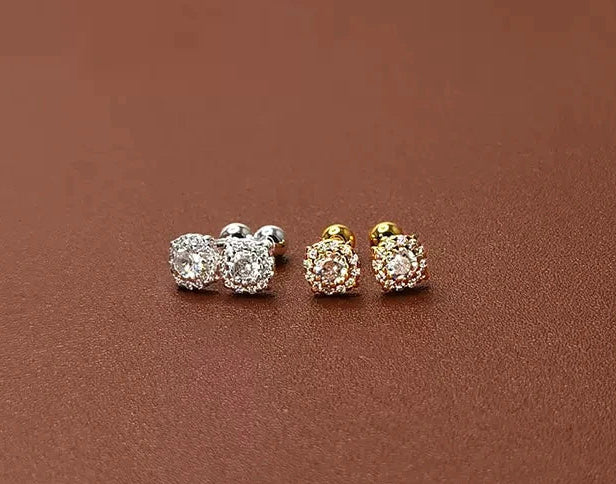 Three pairs of earrings in silver, gold, and rose gold on a brown surface.