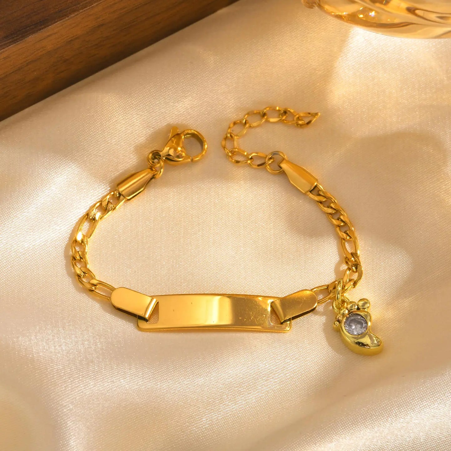 Gold bracelet with a tag and small charm on a beige fabric background