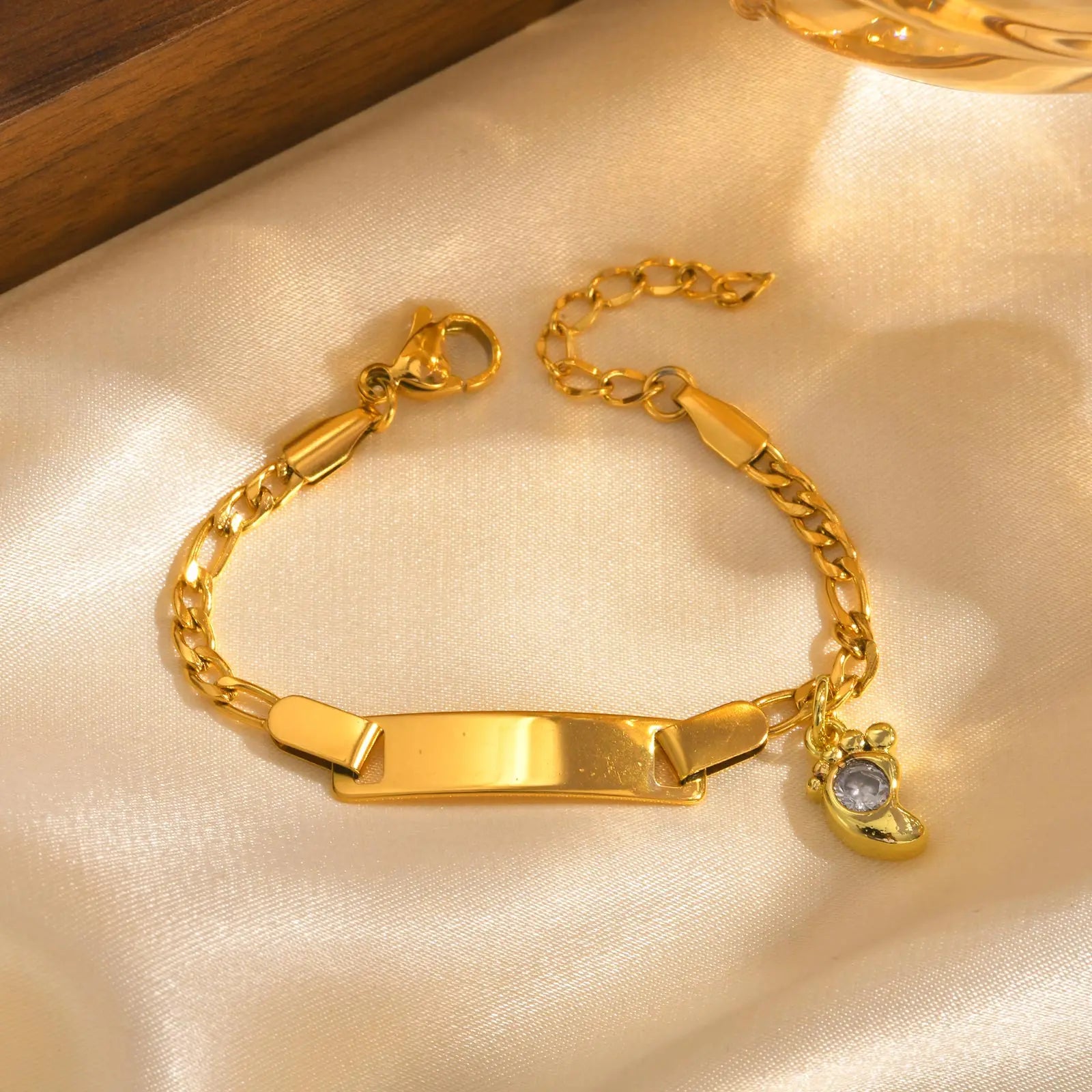 Gold bracelet with a tag and small charm on a beige fabric background